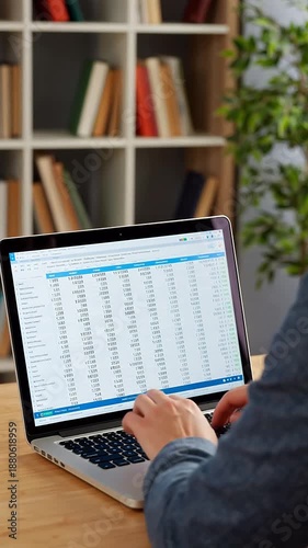 Person typing on a laptop with financial data displayed on the screen, in a home office setting
