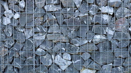 A fragment of a gabion with a metal cage filled with large gray boulders, the hard, solid texture of stone and metal, a view of a finished gabion with natural rock filling behind an iron grate