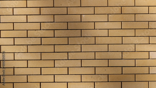 Light brown brick smooth wall in sunny soft lighting with spots of smooth shadows on the surface, geometric textured background of rectangular beige blocks