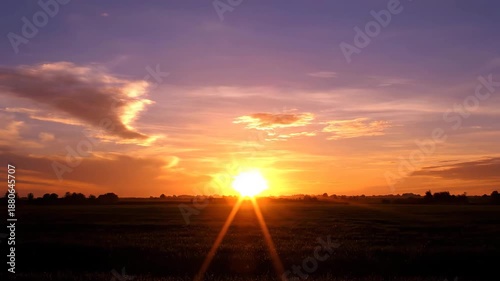 Sunset over open landscape with glowing sun near horizon and warm sky colors. Peaceful natural scene shows calm atmosphere, light rays and tranquil countryside view.