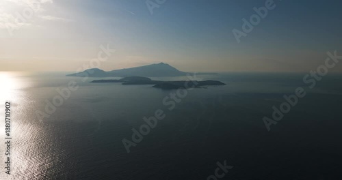 Aerial view of Ischia and Procida islands surrounded by the tranquil sea, with the sun's rays creating a shimmering effect on the water, Capo Miseno, Campania, Italy.