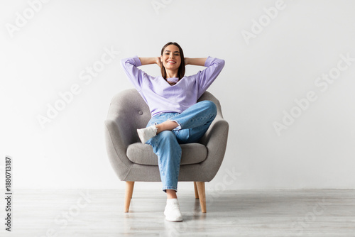 Foto Happy peaceful young woman sitting in armchair with hands behind head, resting, having break from work against white studio wall, full length