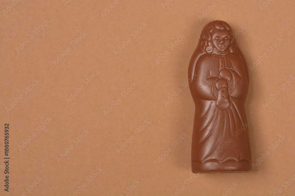Fototapeta premium Milk chocolate figurine shaped like an angel with a flute isolated on a light brown paper background with copy space