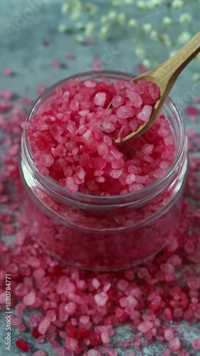 Bright pink salt in a jar with wooden spoon on a gray surface filled with loose salt crystals