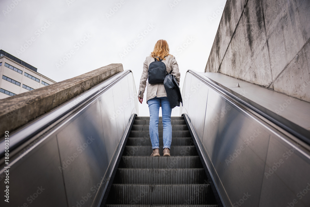 Ταπετσαρία Woman with laptop bag and backpack commuting to work on escalator in urban area
