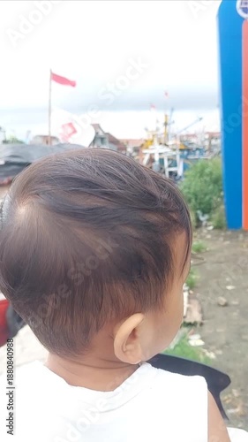 A little boy stood with an innocent and curious gaze, looking at a row of boats slowly moving along the river.