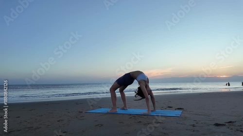Lesbian woman practicing wheel pose yoga at sunset beach