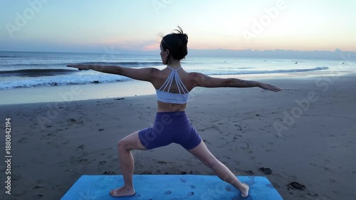 Lesbian woman performing warrior two yoga pose on the beach at sunrise