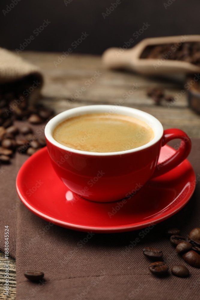 Fototapeta premium Cup with aromatic coffee, beans and napkin on wooden table, closeup