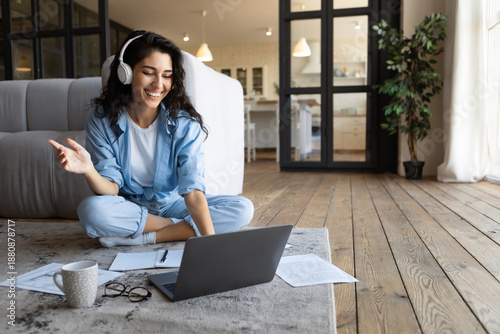 Photos Happy millennial woman in headphones communicating online on laptop, taking part in webinar from home, free space