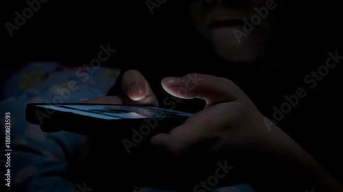 Close-up of a woman using a smartphone in a dark bedroom, browsing the internet and scrolling the screen with her finger. Close-up of a female hand scrolling on a mobile phone in a dimly lit room. 