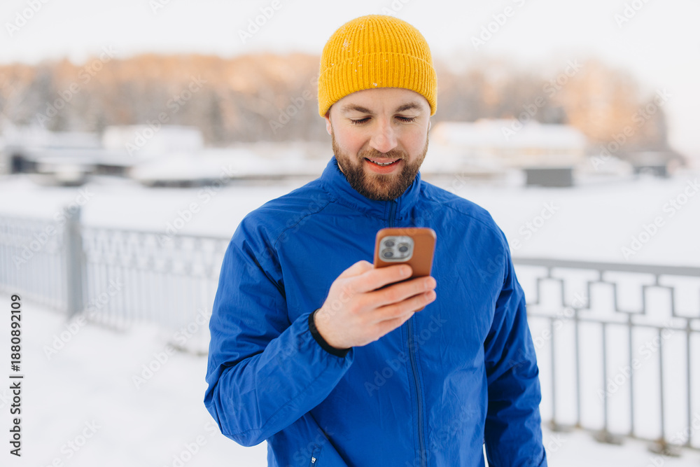 Fototapeta premium Man checking smartphone for navigation or fitness tracking while exercising outdoors in snowy winter park