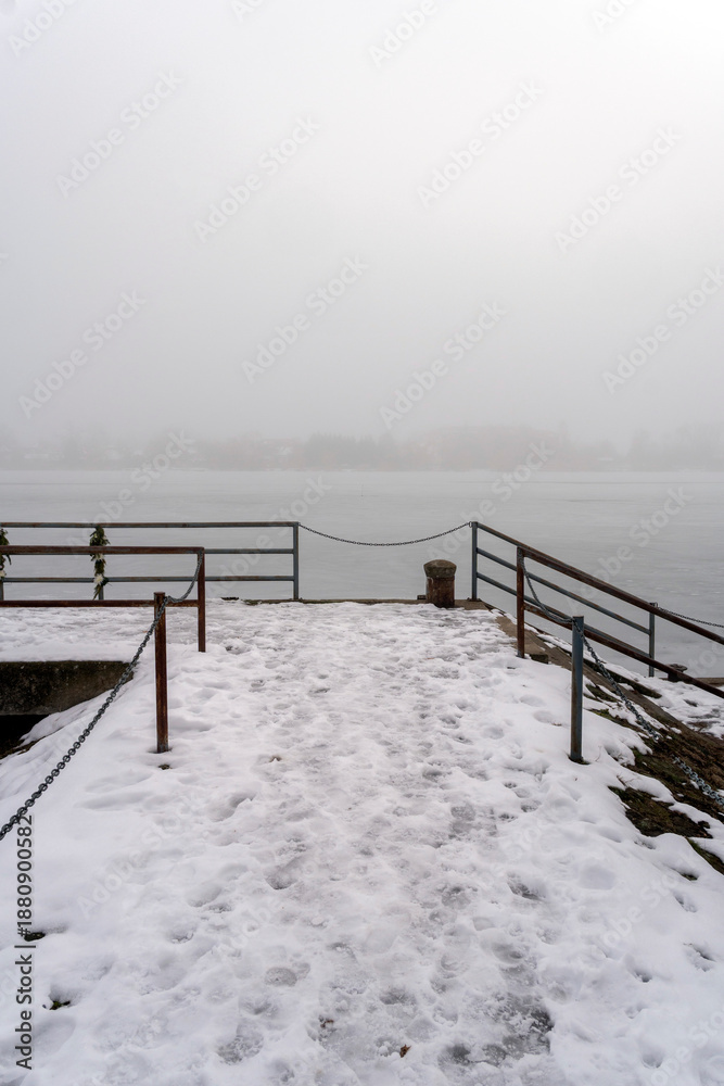 Fototapeta premium Snow covers a pier near a lake with fog surrounding the area during winter in a quiet, remote location