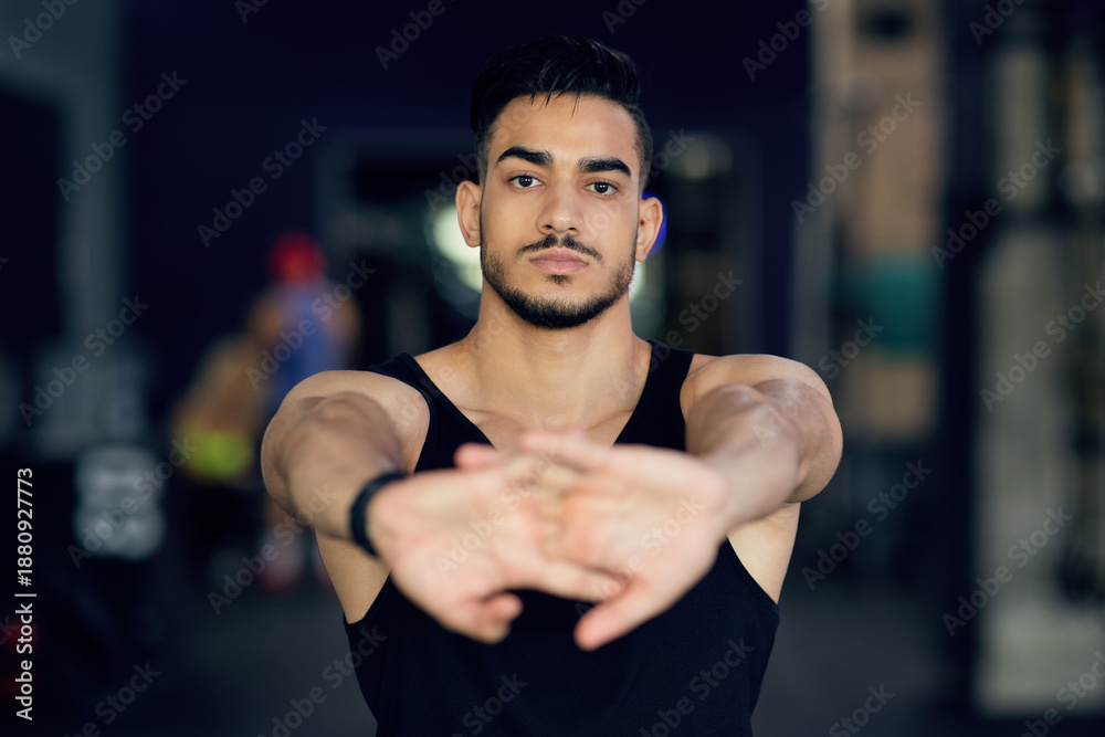 Fototapeta premium Portrait Of Sporty Young Arab Man Stretching Arms At Camera, Confident Middle Eastern Male Athlete Warming Up Before Training At Gym, Ready For Fitness Workout, Closeup Shot, Selective Focus