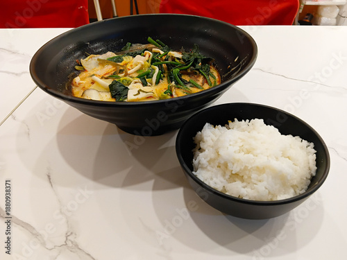 Spicy mala soup served in a black bowl, filled with vegetables and herbs, rich chili broth, hot flavor, Asian comfort food style. with rice