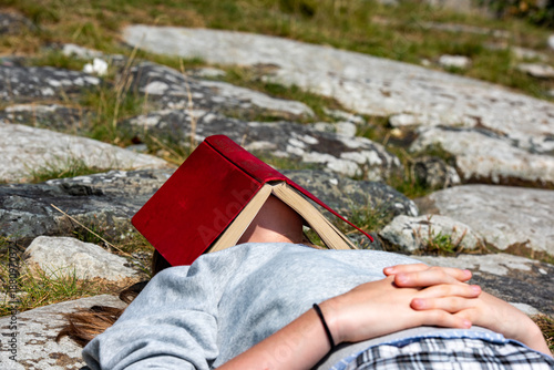 Anonymous bored girl asleep on rocks with a book over her face.