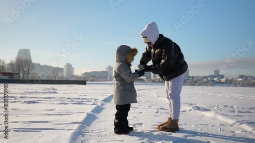A mother in the cold on a sunny day pours hot tea from a thermos for her child.