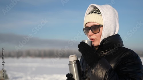 A girl in the cold in sunny weather drinks hot tea from a thermos
