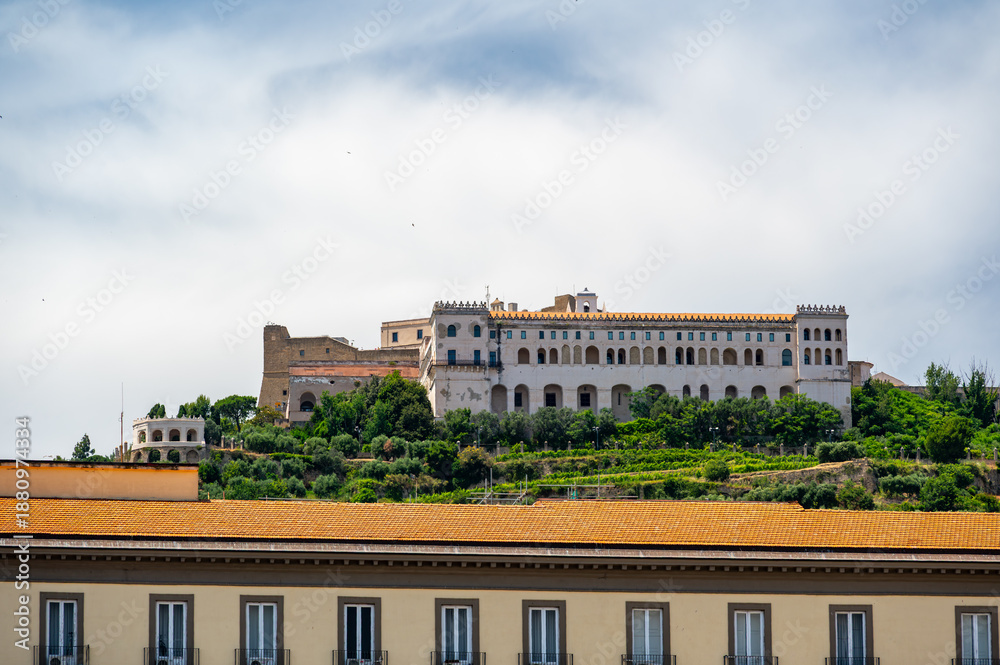 Fototapeta premium View of Castel Sant Elmo from below in Naples, Italy, showing the fortress towering above the city with its massive stone walls and historic hilltop presence.