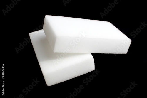 On a black background lie two white melamine sponges for cleaning the house.