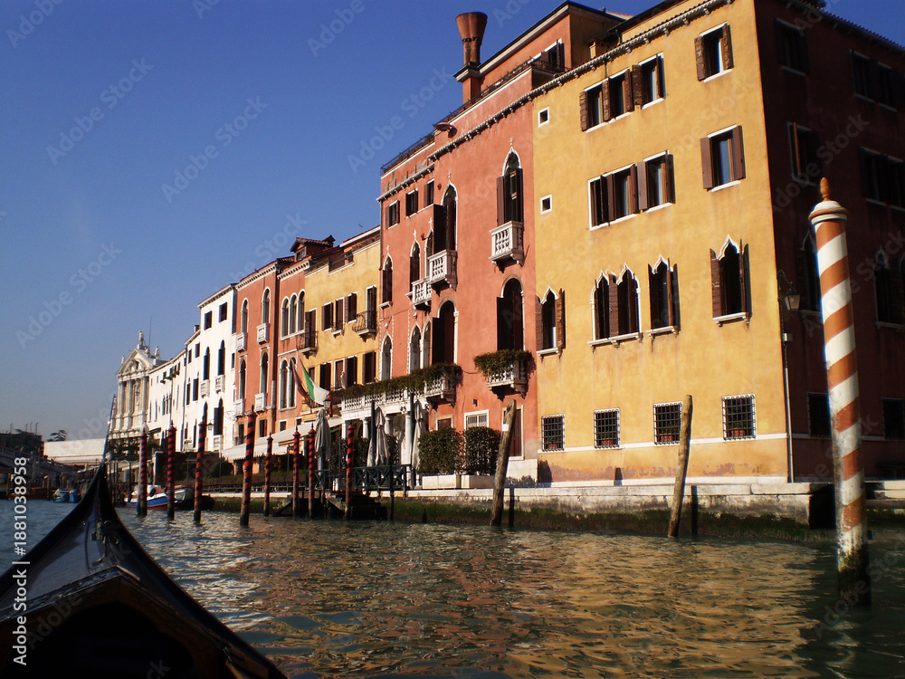 Obraz premium Drifting quietly along Venice s winding canals, a traditional gondola passes beneath arched bridges and alongside elegant historic buildings worn smooth by time and water. The gentle rhythm of the oar