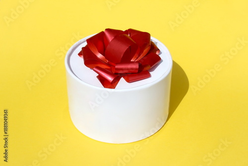 On a yellow background there is a round white gift box with a bow.	
