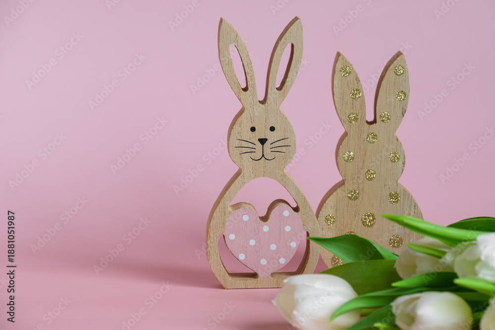 Obraz premium Wooden Easter bunnies on a delicate pink background with white tulips. Theres room for text.