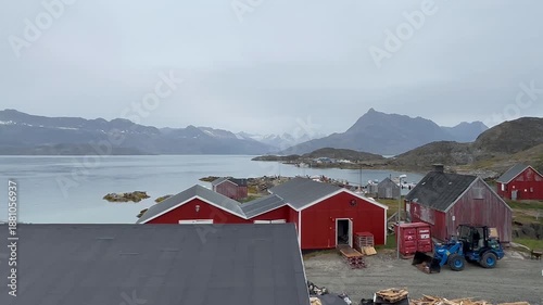 A scenic view of Tasiilaq village nestled among towering mountains in eastern Greenland. Colorful houses contrast with rugged rocky peaks and the vast Arctic landscape