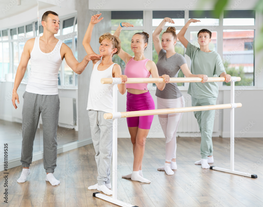 Fototapeta premium Slim adolescent attendees of ballet courses training third position under control of ballet-master in dancehall