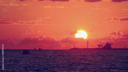 Number 3. Dramatic red-orange sunset, with the outline of coastline and ships and sailboats floating on water visible on horizon. Not AI