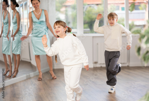 Smiling preteen girl practicing vigorous jitterbug moves with boy partner during dance lesson in choreography studio under guidance with female teacher..