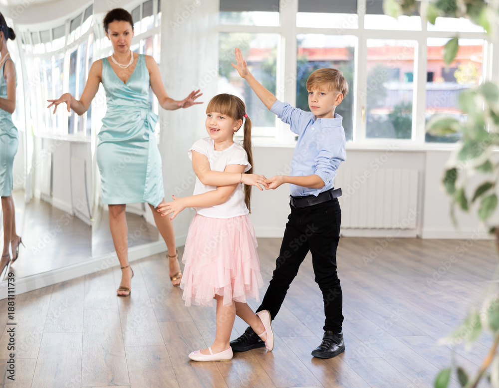 Obraz premium Boy paired up with girl during ballroom dancing lesson. Children rehearse waltz while female teacher conduct dance class