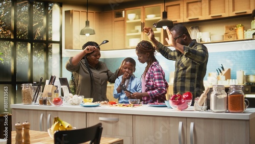 Φωτογραφία Black parents and kids having fun singing and dancing in the kitchen, cooking homemade pizza and acting goofy for the bonding weekend activity