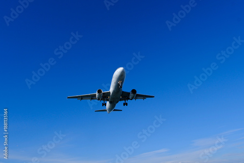 White commercial airplane approaching against clear blue summer sky. Commercial airliner coming in for landing, blue summer sky background
