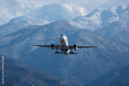 Takeoff with Stunning Mountain Backdrop. White airplane taking off against snow-capped mountains, clouds and a blue sky.