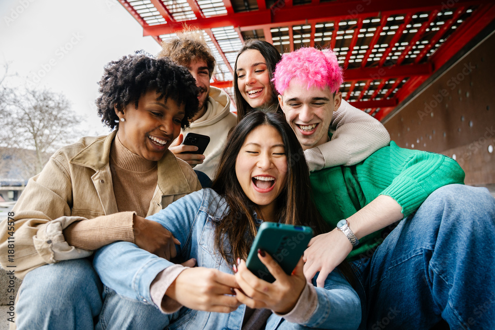 Fototapeta premium Young group of people having fun while hanging out and using mobile phones sitting together outdoor