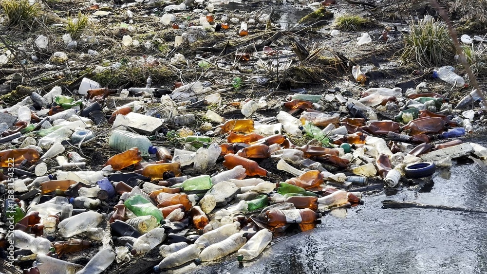 Obraz premium Dirty river is polluted with many plastic bottles. A lot of trash is dumped in open and freely available places at nature. Global environmental pollution problem. Concept of ecological disaster