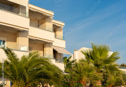 Scenic view of white mediterranean apartments surrounded by palm trees against clear sky, with copy space. Concept of summer vacation, seaside resort, tropical garden, real estate, holiday destination