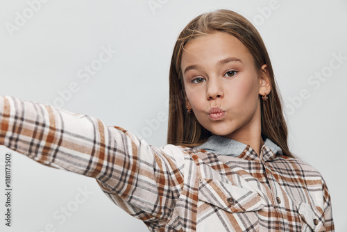 Obraz na plátně Teenage girl with long hair wearing plaid shirt making a selfie with pout lips on white background