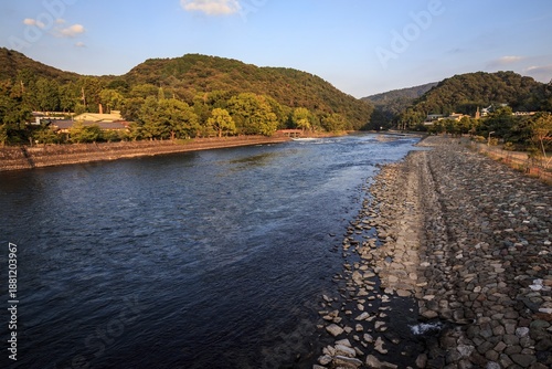 Fotografija Late Afternoon Sun Over the Uji River with Forested Mountains and Stone Embankme