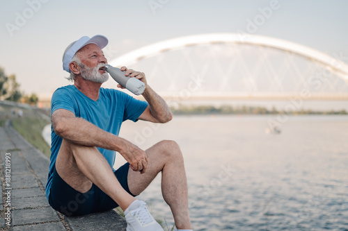Tableau sur toile Senior athlete drinking water after exercising by the river