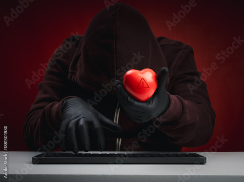 Foto Romance scam concept showing anonymous hacker in dark hoodie holding red heart with warning icon, symbolizing online love fraud, emotional manipulation, and cyber deception in dating scams