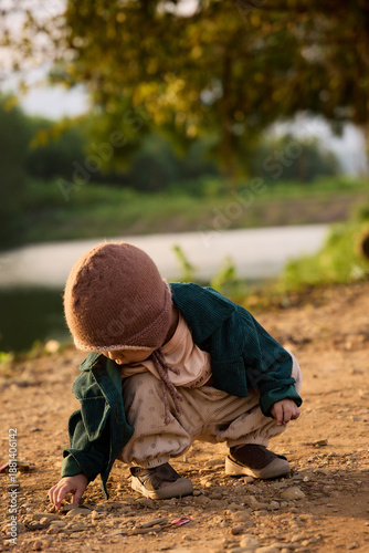 The toddler hunched over on the sandy shore, concentrating on his play near the water