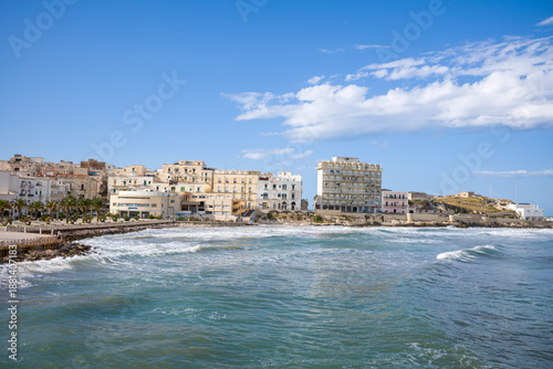 Cuadro en lienzo Clustered pastel buildings line the rocky shoreline of Vieste, Italy, facing gentle Adriatic waves under a bright blue sky