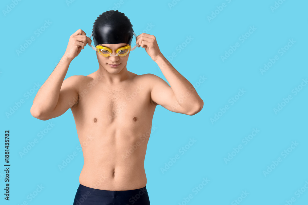 Obraz premium Young male swimmer with goggles on blue background