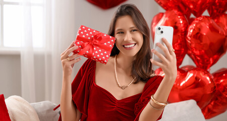 Beautiful young woman with gift taking selfie at home. Valentine's Day celebration