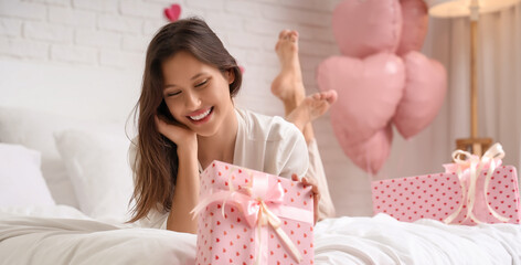 Beautiful young woman with gift and shopping bags lying on bed in bedroom. Valentine's Day celebration
