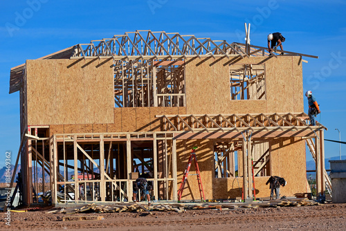 Construction crew framing a two story wooden home under construction, representing residential housing development, structural assembly, and active jobsite building operations