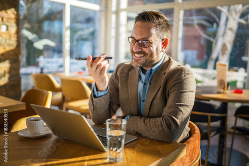 Photography Smiling man recording voice message on smart phone in cafe