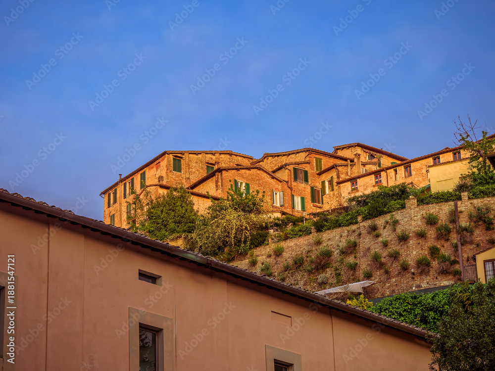 Fototapeta premium Old houses perch on a scenic cliff near Siena’s historic center, blending into the Tuscan landscape. A cultural travel in Italy.